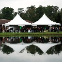 Two large wedding tents are reflected in a lake.